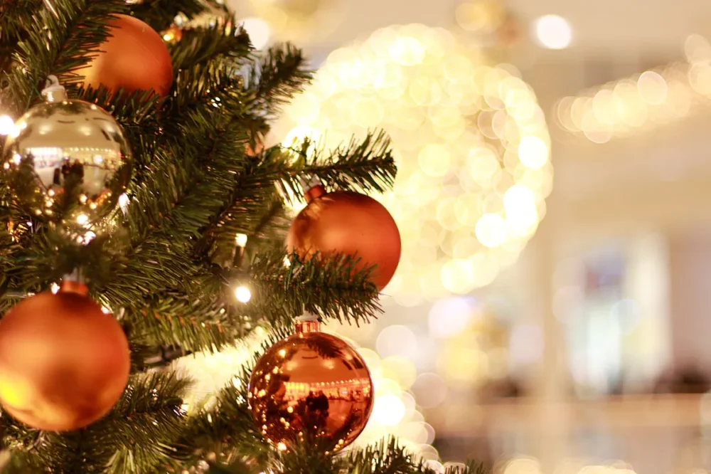 Nahaufnahme eines festlich geschmückten Weihnachtsbaums mit goldenen und roten Kugeln, im Hintergrund warme Lichter.